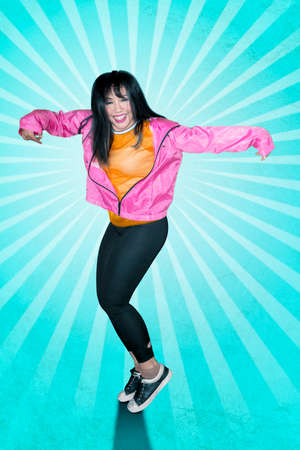 Joyful female hip-hop dancer is dancing with blue background in the studio