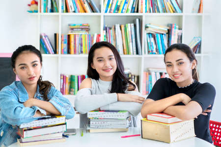Group of teenage girls smiling at the camera while studying in the library with bookcase backgroundの写真素材