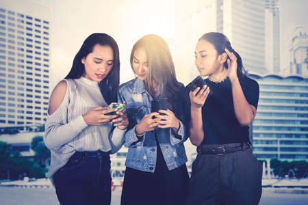 Group of teenage girls using their cellphone while standing together on the roadside with sunlight backgroundの写真素材