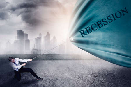Caucasian businessman using a chain to pull a fabric with recession word at outdoor with misty city backgroundの写真素材