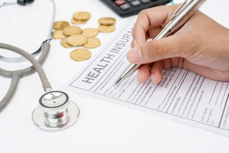 Close up of unknown man hand filing a health insurance claim application with a pen and calculator...