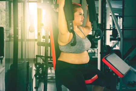Blonde fat woman wearing sportswear while exercising with a fitness machine in the gym center on...