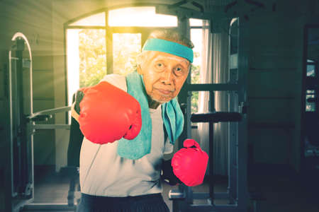 Old man showing his punch while exercising in the fitness center with sunlight background