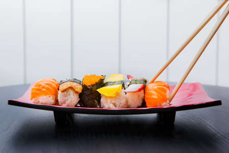 Close up of chopsticks holding a tasty sushi of salmon on a plate over the tableの写真素材