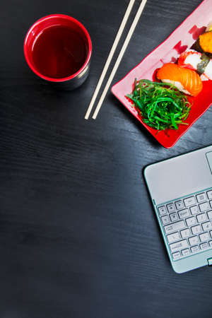 Top view of laptop with sushi sashimi set and soy sauce on the red plate with copy space on the tableの写真素材