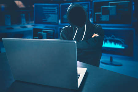 Unrecognizable hacker looks thinking with laptop on desk and coding background