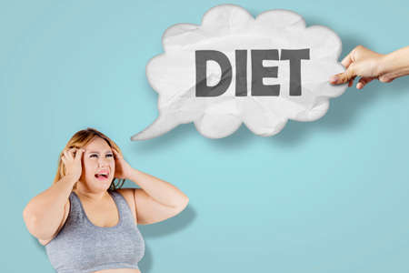 Stressed fat woman looking at diet word on a cloud bubble speech while standing in the studioの写真素材