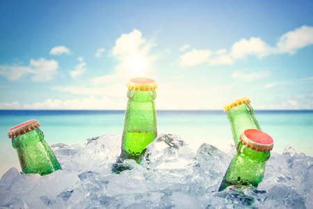 Close up of five frosty beer bottles in stack of ice cubes under blue sky. Shot in the tropical beachの写真素材
