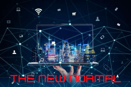 Unknown hand holding a laptop and new normal text with smart city and network connection at night