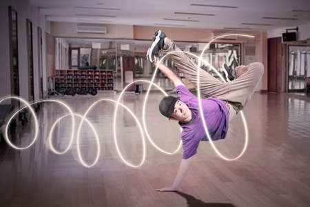 Young man jumping while performing break dance in the studio with green screen background