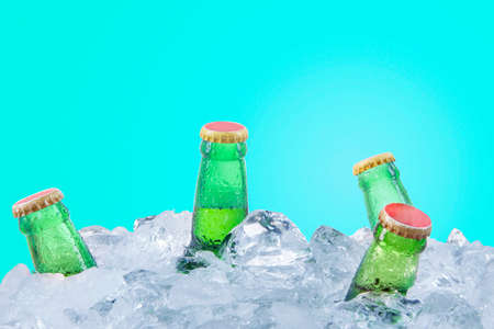 Five frosty beer bottles in stack of ice cubes in the studio with blue color background