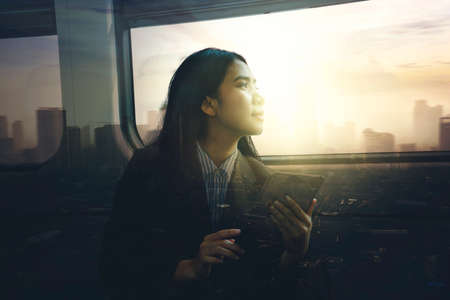 Double exposure of pensive woman using a digital tablet while sitting on the train with sunset backgroundの写真素材