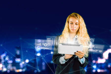 Blonde businesswoman using a digital tablet with virtual growth graphs screen while standing with...