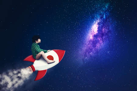 Cute little boy riding a rocket while flying on the night sky with stars and milky way background