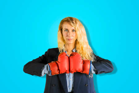Blonde businesswoman wearing boxing gloves while threatening someone and standing in the studioの写真素材
