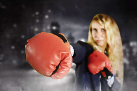 Close up of red boxing gloves wore by blonde businesswoman while punching at the camera and standing...