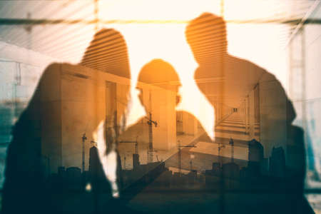Double exposure of three engineers working together with silhouette of buildings construction backgroundの写真素材