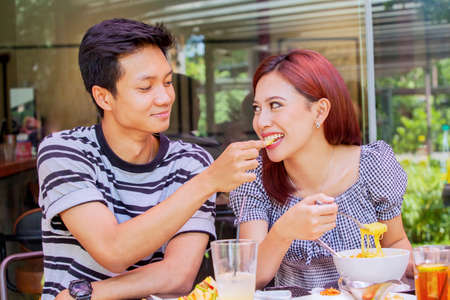 Romantic young man feeding his girlfriend while having lunch together in the restaurant with tasty...