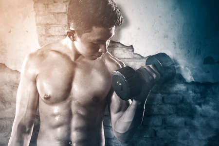 Muscular young man exercising with a dumbbell while standing with grunge backgroundの写真素材