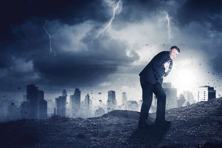 Male manager looks scared while embracing a suitcase while standing with storm city backgroundの写真素材