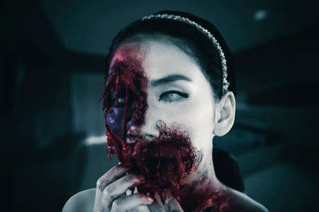 Halloween horror concept. Close up of spooky woman with wounded face sitting in the dark bedroomの写真素材