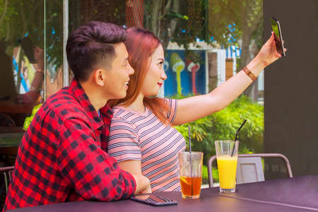 Happy young couple taking selfie photo with a mobile phone while dating in the cafeの写真素材
