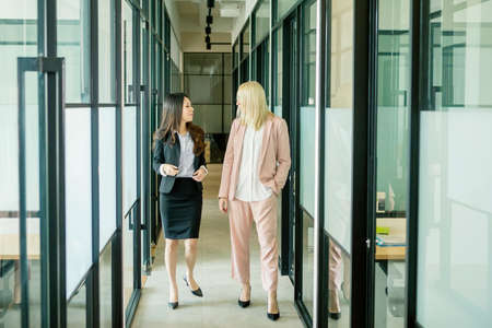 Two happy businesswoman talking and discussing while walking together in the office corridorの写真素材