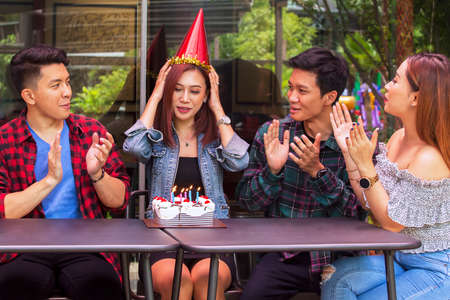 Group of young people clapping hands and singing together while celebrating a birthday party for...