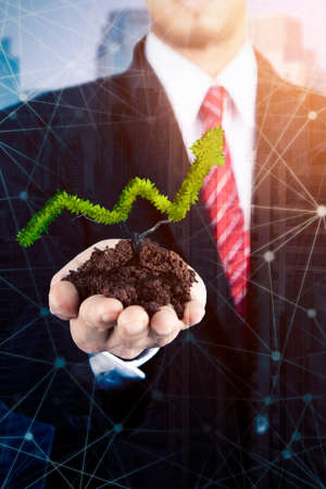 Double exposure of businessman hand holding a plant shaped an arrow upward symbol while standing...