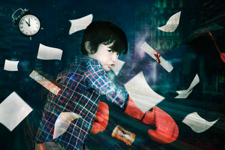 Double exposure of little boy wearing boxing gloves while throwing paper and diploma with night city backgroundの写真素材