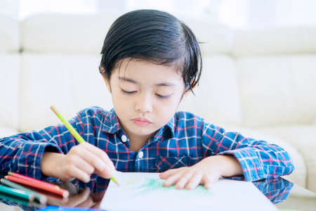 Little boy drawing with colored pencil while doing self quarantine at home to prevention Coronavirus pandemicの写真素材