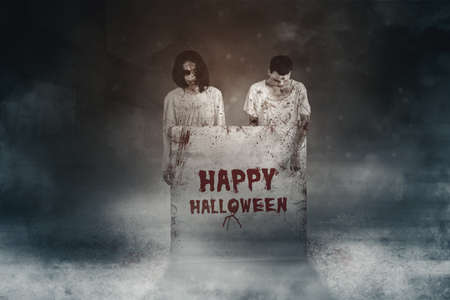 Two spooky ghosts showing a stone with happy halloween text in the grave. Concept of Halloween...