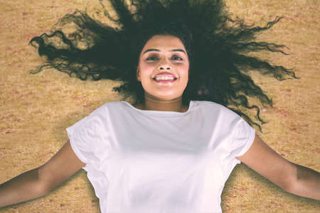 Top down view of young woman smiling at the camera while lying down on the dried grass at the autumn...