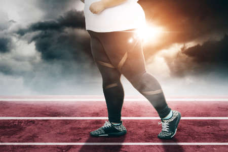 Close up of fat woman feet running on the track line with sunlight on cloudy sky backgroundの写真素材
