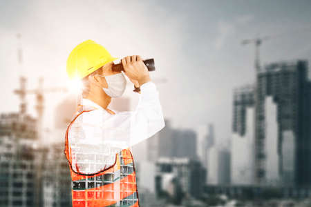 Double exposure of male engineer using binoculars with skyscraper project background