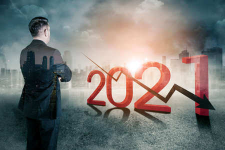 Double exposure of confident businessman standing near 2021 numbers and declining arrow with modern city backgroundの写真素材
