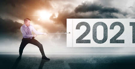 Side view of Caucasian businessman using a chain to pull a fabric with 2021 numbers in cloudy sky backgroundの写真素材