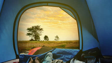 Young woman feet lying in tent with dawn sky view at sunrise time while camping in the forest
