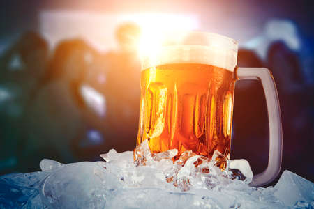 Close up of fresh beer in a big glass with silhouette of happy people dancing in nightclub