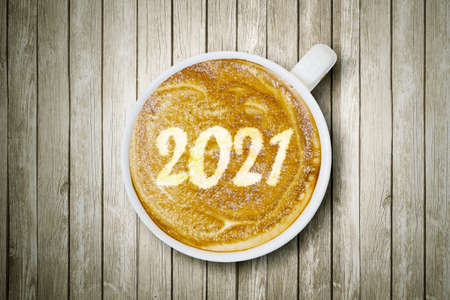 Close up of number 2021 on frothy surface of cappuccino served in a cup above wooden tableの写真素材