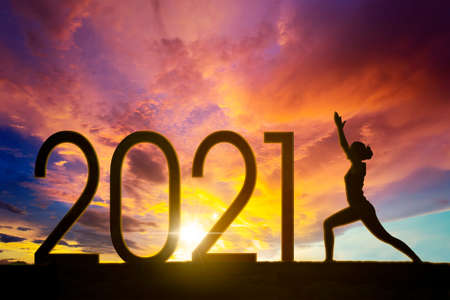 Silhouette of young woman exercising yoga with number 2021 at sunrise time. Shot at natureの写真素材