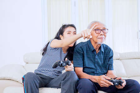 Young woman playing video games with her father while sitting on the sofa. Shot at homeの写真素材