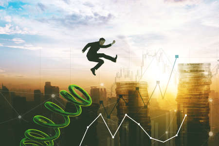 Double exposure of Caucasian businessman using a spring to jumping above growth business chart and coins on modern city backgroundの写真素材
