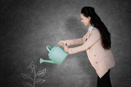 Caucasian businesswoman looks happy while watering a drawn plant on the blackboard with a water can