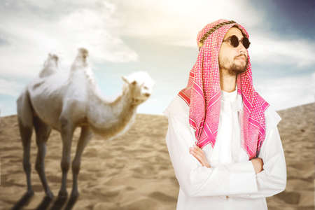 Confident businessman wearing sunglasses while standing near a camel on the desertの写真素材
