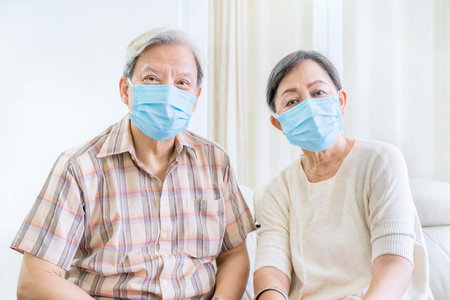 Close up of old couple wearing medical mask to prevention coronavirus spread while sitting on the couch. Shot at homeの写真素材
