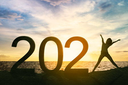 Silhouette of young woman expressing happy while jumping with 2021 numbers on the beach with sunrise backgroundの写真素材
