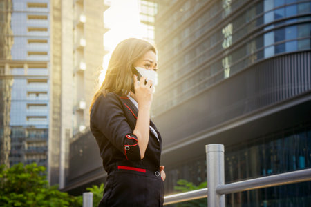 Young businesswoman wearing a face mask and making a phone call while standing on the pedestrian bridgeの写真素材