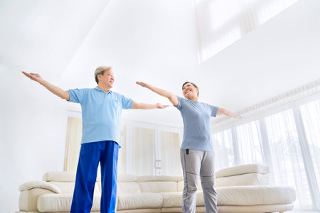 Low angle view of happy old couple wearing sportswear while exercising together in the living room. Shot at homeの写真素材