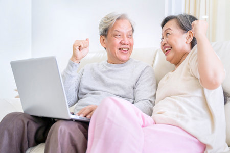 Smiling old couple using a laptop computer together at home while sitting together on the sofaの写真素材